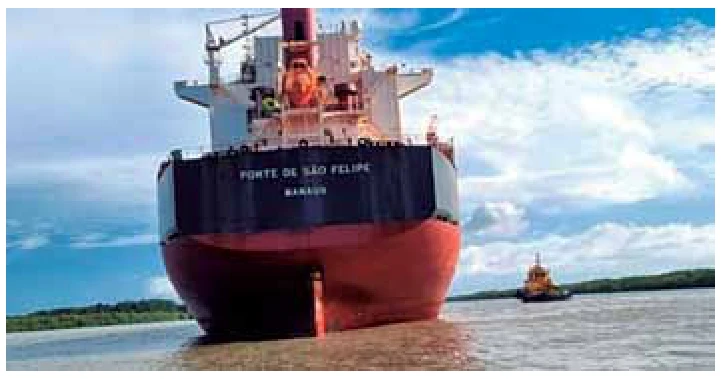 Navio mercante Forte de São Felipe visto de popa, em águas calmas, com um rebocador ao fundo