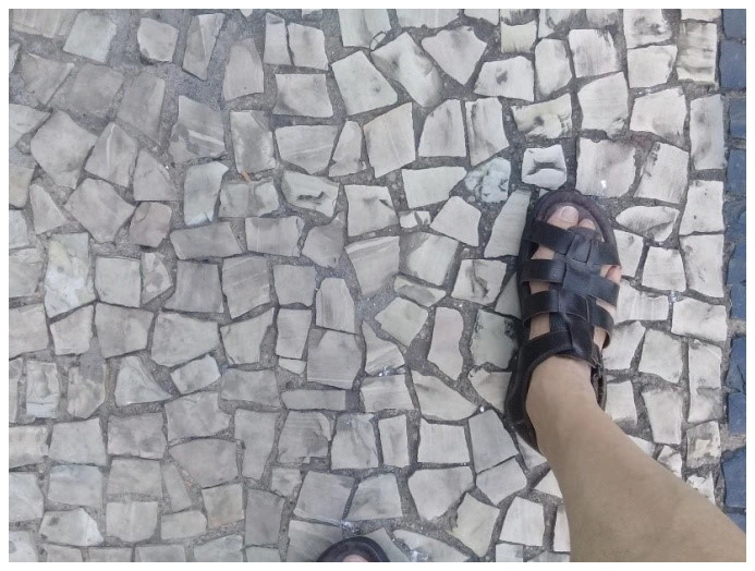Pé de uma pessoa de calçado número 40 sobre piso de pedras portuguesas