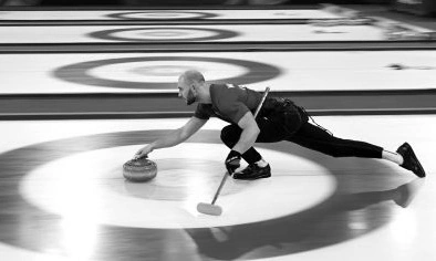 Atleta lançando uma pedra de curling em pista de gelo