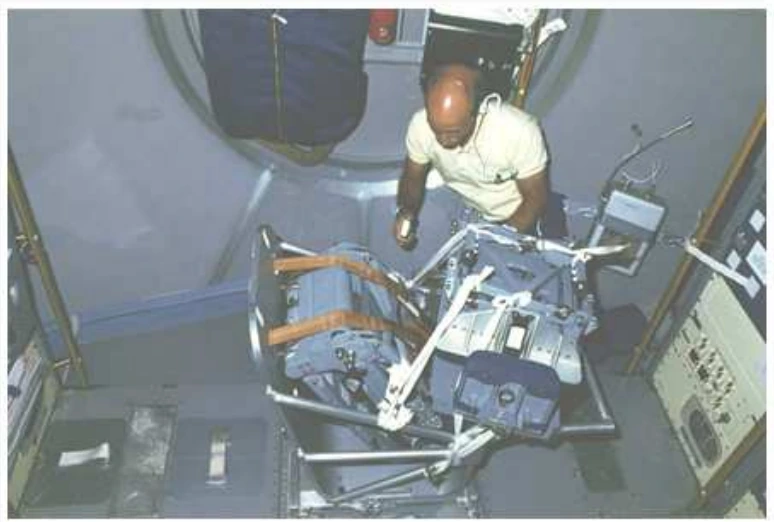 Astronauta utilizando o Body Mass Measuring Device, cadeira sobre molas para medir massa em microgravidade