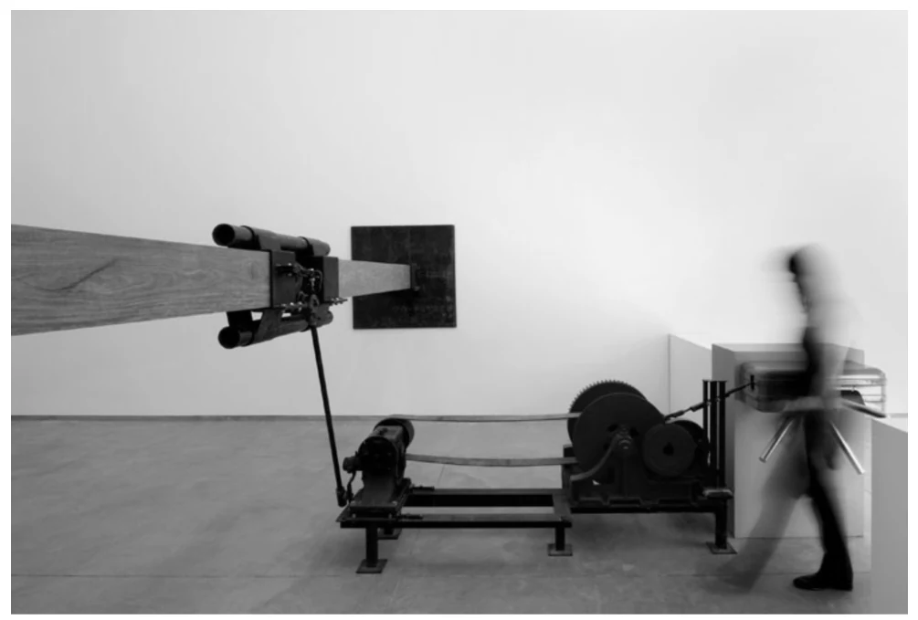 Fotografia da instalação Samson, de Chris Burden, com um macaco mecânico e uma viga de madeira pressionando a parede.
