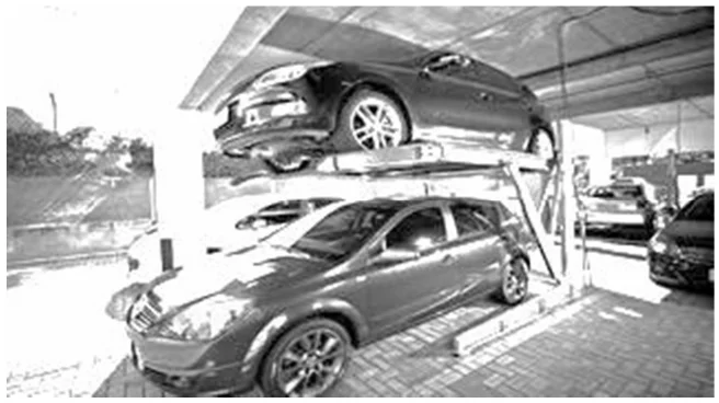 Fotografia de um elevador hidráulico duplicador de vagas: um carro estacionado sobre a plataforma elevada e outro no piso inferior