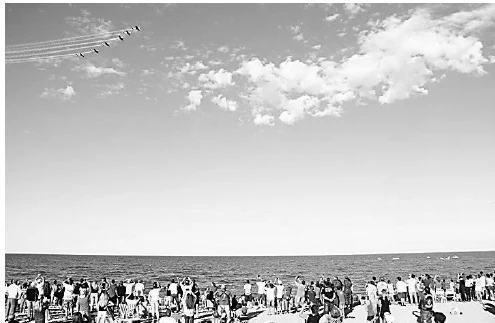 Fotografia de uma multidão na praia olhando para o céu, onde passam aviões da esquadrilha da fumaça