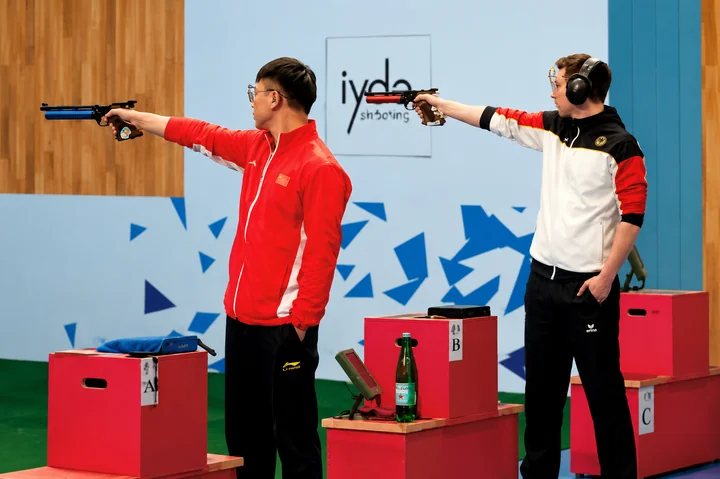 Atletas competindo em prova de tiro esportivo com pistolas de ar comprimido, mirando em direção ao alvo