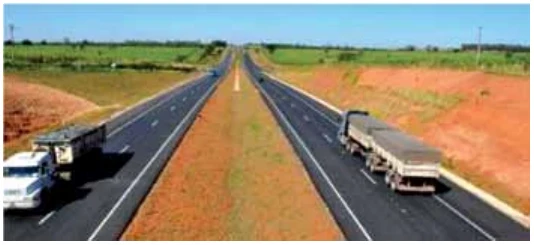 Fotografia de uma rodovia de duas pistas paralelas, vista de cima, com um caminhão em cada pista, um vindo para o observador e o outro se afastando.