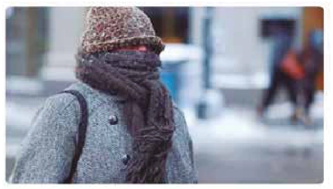 Pessoa com casaco, gorro e cachecol cobrindo o corpo e parte do rosto em ambiente frio.