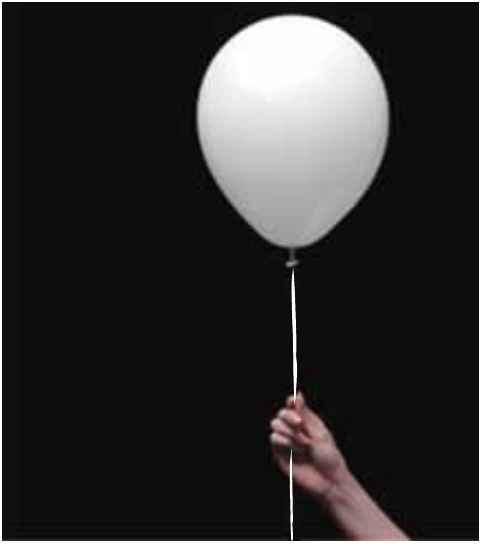 Fotografia de uma mão segurando pelo fio um balão cheio de gás hélio, sobre fundo escuro